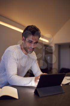 Evening Shot Of Man In Kitchen Working Or Studying From Home Using Digital Tablet