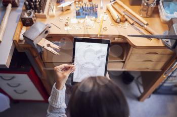 Overhead View Of Female Jeweller Comparing Ring With Drawn Design On Digital Tablet In Studio