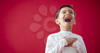 Portrait Of Laughing Young Boy Against Red Studio Background Smiling At Camera