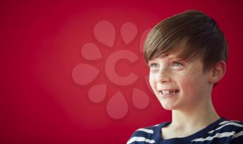Portrait Of Smiling Young Boy Against Red Studio Background