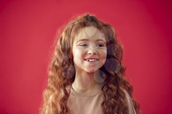 Portrait Of Girl With Long Red Hair Against Red Studio Background Smiling At Camera
