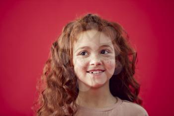 Portrait Of Girl With Long Red Hair Against Red Studio Background Smiling At Camera