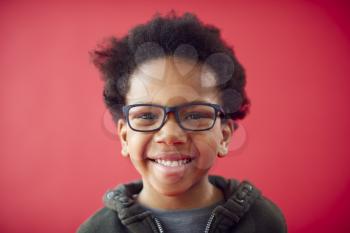 Portrait Of Smiling Young Boy Wearing Glasses Against Red Studio Background