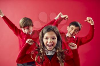 Portrait Of Excited Elementary School Pupils Wearing Uniform Having Fun On Red Studio Background