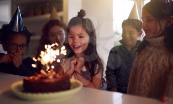 Girl Celebrating Birthday With Group Of Friends At Home Being Given Cake Decorated With Sparkler