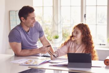 Father Helping Daughter With Homework Sitting At Kitchen Counter Using Digital Tablet Together