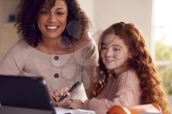Mother Helping Daughter With Homework Sitting At Kitchen Counter Using Digital Tablet Together