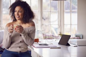 Woman With Digital Tablet Working From Home On Kitchen Counter Drinking Coffee