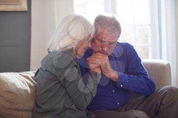 Woman Sitting On Sofa Comforting Senior Man Suffering With Mental Health Issues At Home