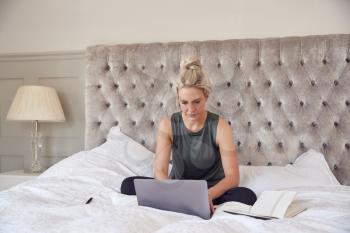 Businesswoman Sitting On Bed With Laptop Working From Home On Video Call During Pandemic Lockdown