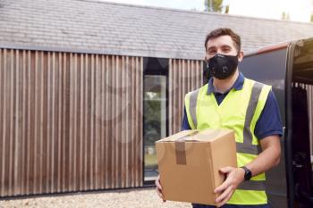 Portrait Of Delivery Driver Wearing Mask Holding Package Outside House