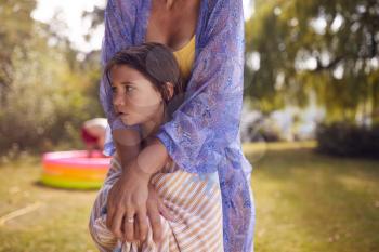 Mother Wrapping Daughter In Towel As Family Play With Water In Summer Garden
