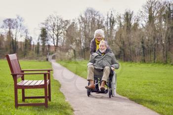 Senior Woman Pushing Senior Man In Wheelchair Outdoors In Fall Or Winter Park