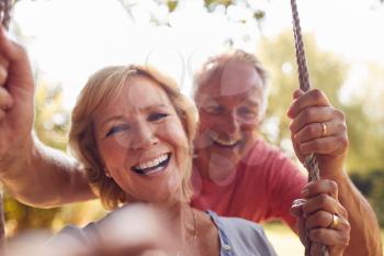 Portrait Of Retired Couple Having Fun With Man Pushing Woman On Garden Swing