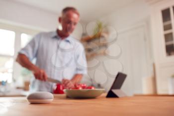 Retired Man Making Meal In Kitchen With Smart Speaker In Foreground