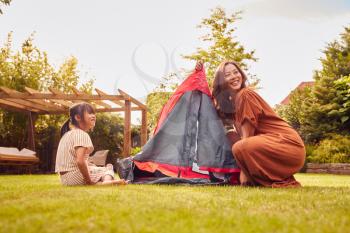 Asian Mother With Daughter In Garden At Home Putting Up Tent For Camping Trip Together