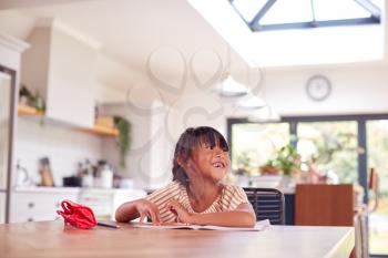 Young Asian Girl Home Schooling Working At Table In Kitchen Writing In Book