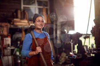Portrait Of Female Blacksmith Holding Hammer Standing In Forge