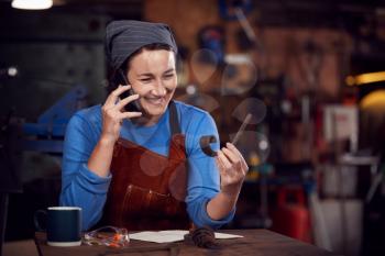 Female Blacksmith Working On Design In Forge Whilst Using Mobile Phone