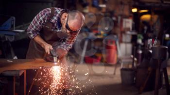 Male Blacksmith Using Plasma Cutter To Cut Shape From Sheet Metal In Forge