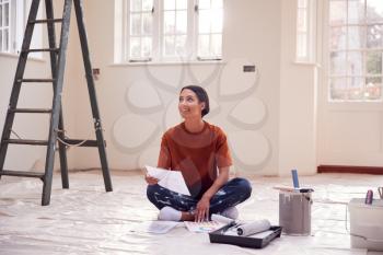 Woman Sitting On Floor With Paint Chart Ready To Decorate New Home