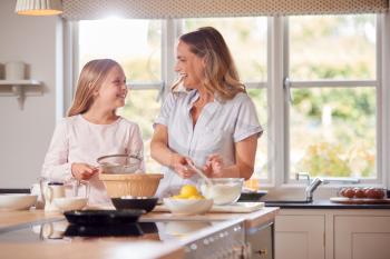 Mother And Daughter Wearing Pyjamas Making Pancakes In Kitchen At Home Together