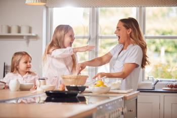 Mother And Two Daughters Making Pancakes In Kitchen At Home Together