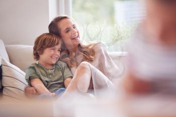 Mother Relaxing With Children On Sofa At Home Watching TV Together