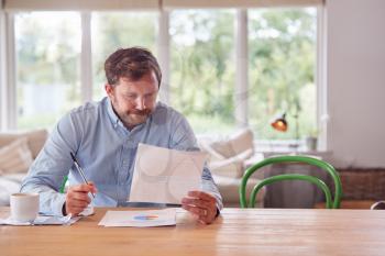 Worried Man Sitting At Table At Home Reviewing Domestic Finances