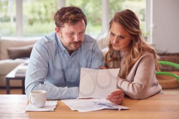 Worried Couple With Bills And Digital Tablet Sitting At Table At Home Reviewing Domestic Finances