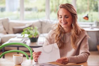 Woman With Digital Tablet Sitting At Table At Home Reviewing Domestic Finances