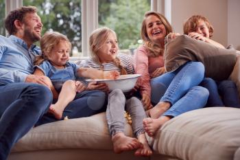 Family Sitting On Sofa At Home Laughing And Watching TV With Popcorn