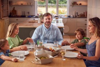 Family Sitting Around Table At Home Joining Hands And Saying Grace Before Meal