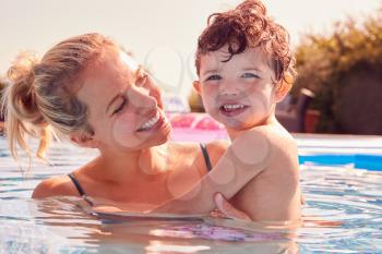 Mother With Young Son Having Fun On Summer Vacation Splashing In Outdoor Swimming Pool