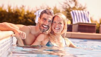 Portrait Of Couple Having Fun On Summer Vacation Relaxing In Outdoor Swimming Pool