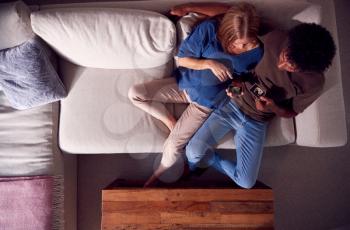 Overhead View Of Couple With Pregnant Woman Looking At Baby Ultrasound Scans On Sofa At Home