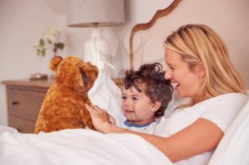 Mother And Young Son Wearing Pyjamas In Bedroom Together Playing With Cuddly Teddy Bear Toy