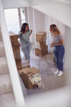 Excited Female Couple Carrying Boxes Through Front Door Of New Home On Moving Day