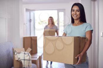 Portrait Of Female Couple Carrying Boxes Through Front Door Of New Home On Moving Day