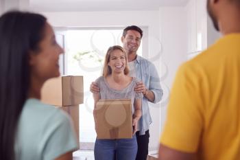 Friends Helping Couple Carry Boxes Through Front Door Of New Home On Moving Day