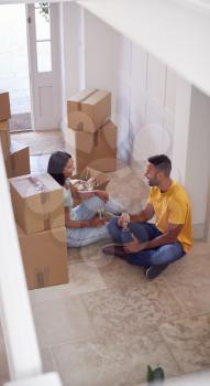 Couple Celebrating With Champagne Sitting On Floor Of New Home On Moving Day