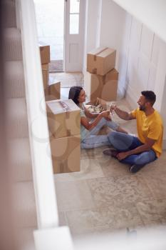 Couple Celebrating With Champagne Sitting On Floor Of New Home On Moving Day