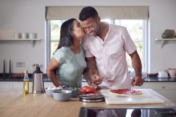 Loving Couple In Kitchen At Home Preparing Homemade Pizzas Together