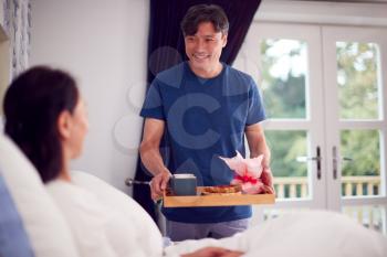 Mature Asian Man Bringing Wife Breakfast In Bed To Celebrate Birthday Or Anniversary