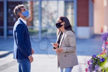 Businessman And Businesswoman Having Socially Distanced Meeting Outdoors In Street