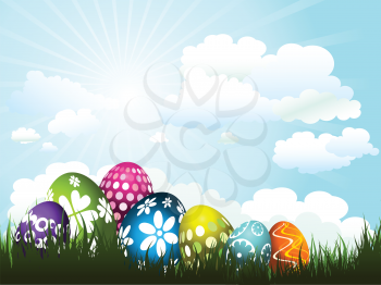 Colourful Easter eggs nestled in grass against a sunny sky

