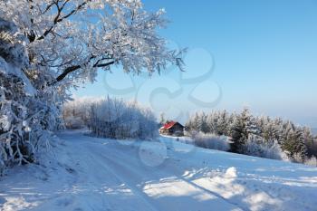 Winter morning in the mountains. Snow-covered road and a small country house with red roof