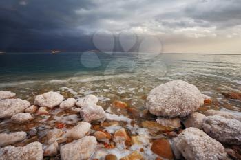 Winter on the Dead Sea. Blue storm cloud, green water and rocks, overgrown with salt