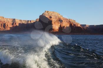 Travel voyage by boat on Lake Powell. Picturesque waves astern the ship. Sunset rays illuminate the rocks on the shore of the lake. Arizona, USA.