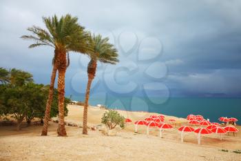 Winter on the Dead Sea. Red umbrellas, green sea and purple thunderheads